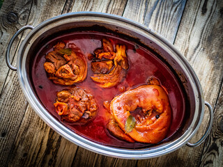 Roast pork knuckle in cooking pan on wooden table