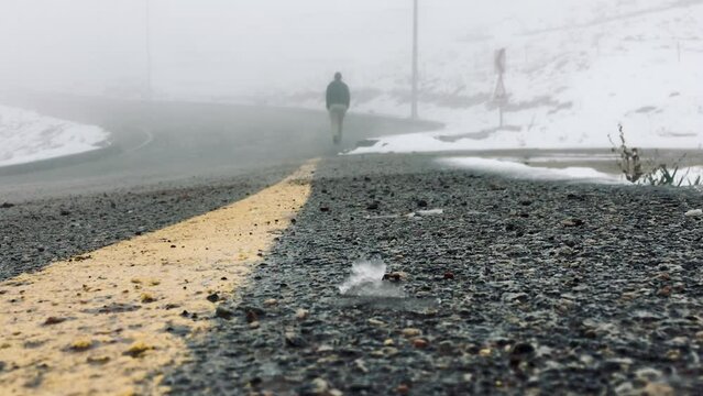 Road focussed near and a man walking on the far blurred side of the foggy road, its snowy but drawing rain