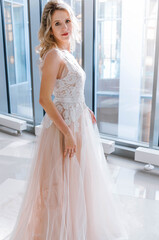 Naklejka premium Beautiful woman in long wedding dress near big window. Bride looking at camera.