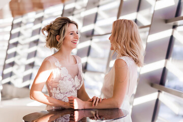 Two blonde model girls posing in  wedding dresses in the interior flooded with sunlight