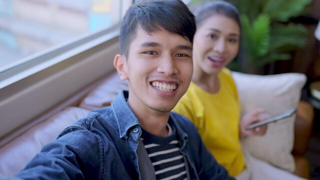 asian husband hand hold smartphone video calling distance connection to friend and family while his wife is waving hand greeting smiling happiness surprise next to him,asian family stay connect call