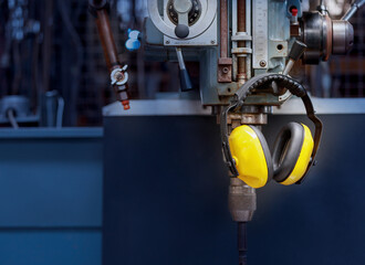 Yellow protective ear muffs hang on machines in heavy industrial plants. - obrazy, fototapety, plakaty