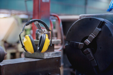 Yellow protective ear muffs hang on machines in heavy industrial plants.