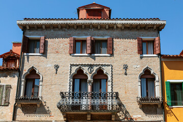 The facade of an old building with Venetian windows and a balcony with a metal decorative lattice on the bank of the canal. Burano Island, Venice, Italy