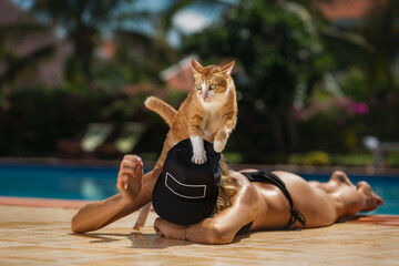 A woman and a cat havving fun near the outdoor swimming pool they are sunbathing