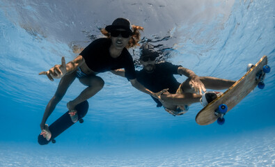 Naklejka premium Man and Woman skateboarding underwater in the swimming pool.