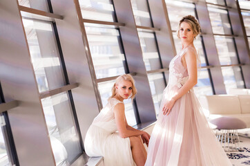 Fototapeta premium Two blonde model girls posing in wedding dresses in the interior flooded with sunlight