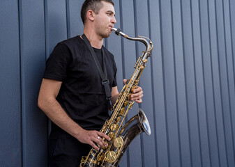 Obraz na płótnie Canvas Young street musician playing saxophone near the big blue wall
