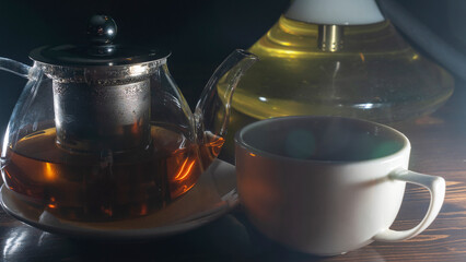 Picture of glass teapot with ceramic cup of green tea on dark background. Hot chinese green tea.
