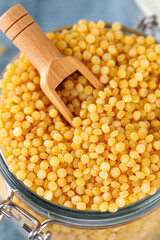 Ptitim. Dry uncooked ptitim pasta close-up in a glass jar with spoon. Israeli couscous