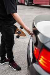 Fototapeta na wymiar Young man in black clothes with longboarding opens the trunk of a black car. Active weekend concept