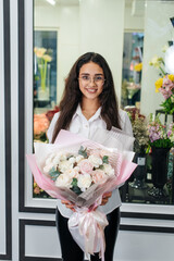 A young girl poses with a beautiful festive bouquet against the background of a cozy flower shop. Floristry and bouquet making in a flower shop. Small business.