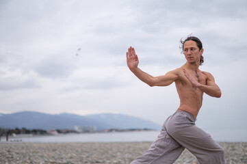 Obraz premium Caucasian man with naked torso practicing wushu on the seashore. 