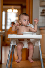 a little boy at home in the kitchen is sitting in a high chair having breakfast, he eats porridge