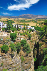 Fototapeta na wymiar View on ancient village Ronda located precariously close to the edge of steep cliff, clear blue sky with fluffy cloud - Andalusia, Spain
