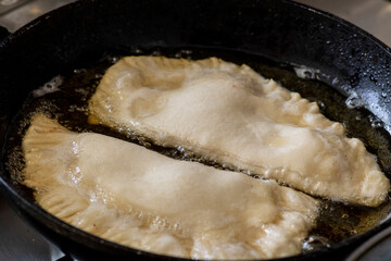 Fried pasties in a frying pan in sunflower oil. Fried dough with meat in oil.