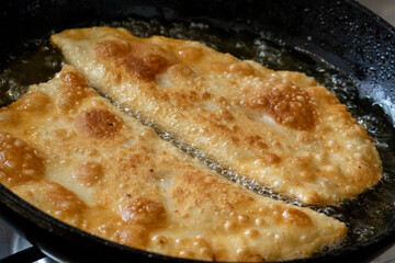 Fried pasties in a frying pan in sunflower oil. Fried dough with meat in oil.