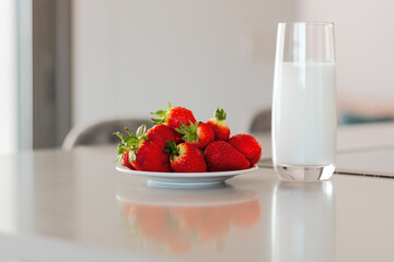 Glass of milk and plate with pile of fresh strawberries set on the table.