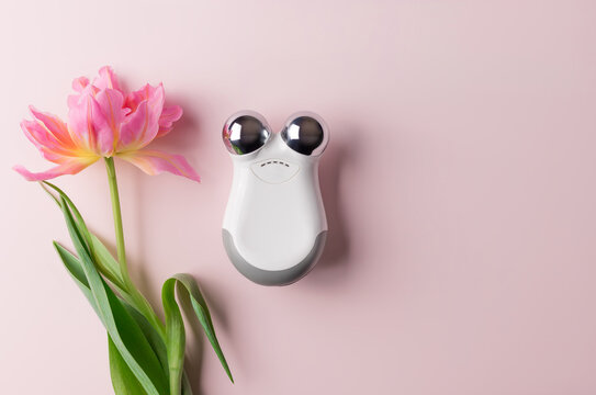 microcurrent facial toning device on pink background with beautiful flower. Facial rejuvenation and facelift with microcurrent therapy
