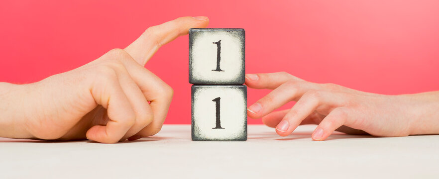 two wooden cubes with the number one and male and female hands on a pink background close-up in the studio