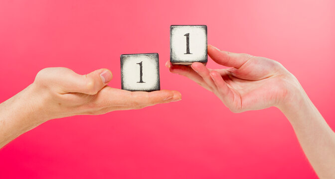 two wooden cubes with the number one and male and female hands on a pink background close-up in the studio - Powered by Adobe
