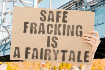 The phrase " Safe fracking is a fairytale " on a banner in men's hands with blurred background. Chemical. Carbon. Behavior. Prohibited. Destruction. Fracture. Exploration. Disaster. Ecosystem. Bad