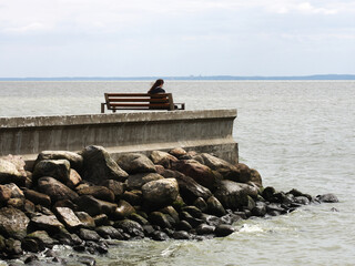 postać człowieka siedzącego na pirsie patrzącego na zatokę