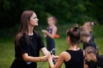 Portrait of coach teaching her trainees to work with clubs on rhythmic gymnastics training outdoors