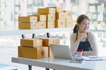 Attractive Asian woman startup small business entrepreneur SME or freelance using a laptop with logistic packaging box.