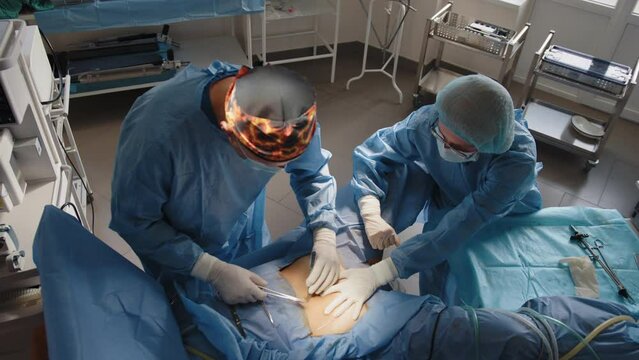 The surgeon uses a needle holder to hold the surgical needle and thread to suture the patient's skin. A team of surgeons stitches the patient's skin using a needle holder and surgical suture