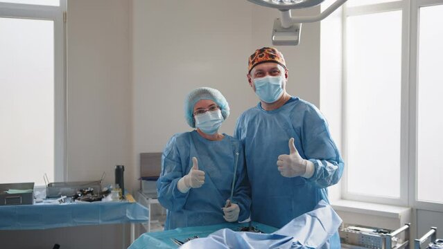 Surgery, medicine and people concept - group of surgeons in operating room at hospital showing thumbs up. Group of surgeons in operating room at hospital showing thumbs up.