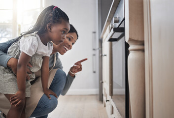 We cant wait to show them to you. Shot of a little girl and her mother sitting in front of the oven.