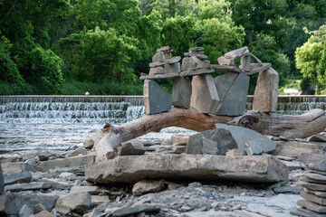 Fototapeta na wymiar A group of rocks is stacked artistically on top of a curved log beside a river and small waterfall in Marie Curtis Park in Toronto, Ontario.
