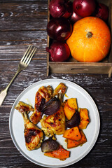 Baked chicken legs with pumpkin and blue onion on a plate.