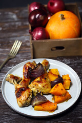 Baked chicken legs with pumpkin and blue onion on a plate.