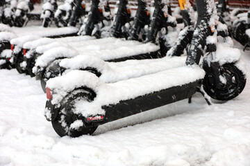 Electric scooters in a row covered with snow on the parking lot. Public e-scooters in snowy weather