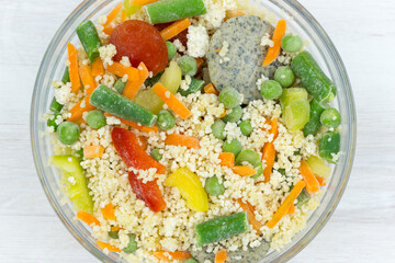 Frozen food: mix of couscous, vegetables and sauce in a glass bowl on a white table