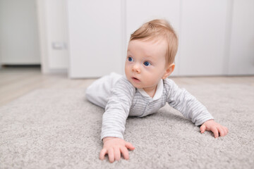 Fototapeta premium Charming newborn baby in a bodysuit lies on his stomach on a soft carpet. Laying out on the tummy. play, child development. space for text. High quality photo