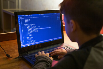 Young boy coding on laptop at night - 496656020