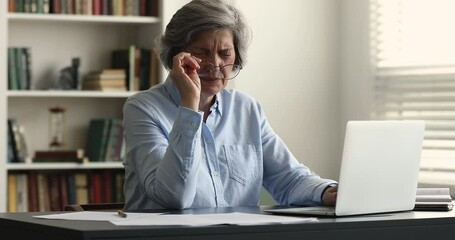 Mature 60s business woman sit at desk feels eyestrain take off eyeglasses rubs fatigued eyes. Long laptop usage, headache, bad blurry vision, eyesight problem, dry eye syndrome, overwork, tech concept