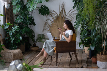 Joyful woman record voice message while remote work from home in house garden with green monstera...