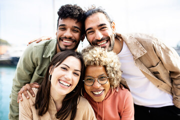 Group portrait of four multiracial united friends outdoors - Friendship concept with millennial guys and girls enjoying day out on city street - Focus on women face - obrazy, fototapety, plakaty