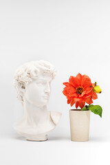 Gypsum statue David's head and blooming flowers in a pot. Minimal creative concept art.