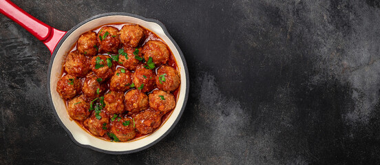 Traditional spicy meatballs in sweet and sour tomato sauce on a dark background. Long banner...
