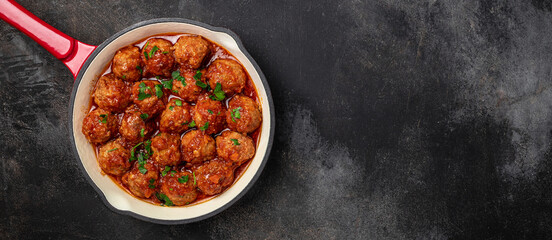 Traditional spicy meatballs in sweet and sour tomato sauce on a dark background. Long banner format. top view