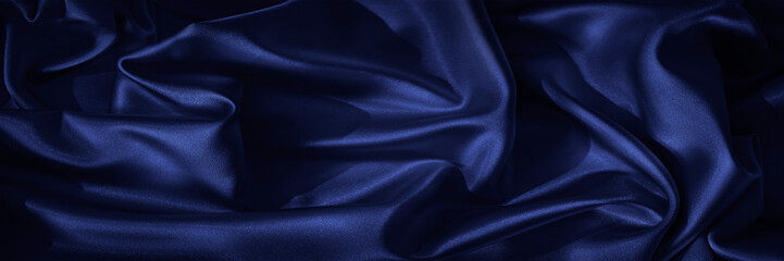 Black blue silk, satin. Shiny fabric surface. Beautiful wavy folds. Dark elegant background with...