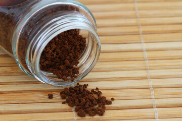 Granules of instant coffee scattered from transparent glass bottle
