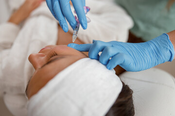 Hands of expert beautician filling female face with hyaluronic acid. Cosmetology concept
