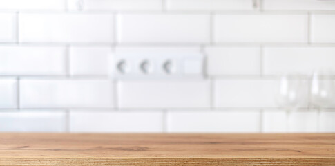 Wood table on blurred background of kitchen space with white tile brick wall on a sunny day. Spring sunlight in the kitchen.