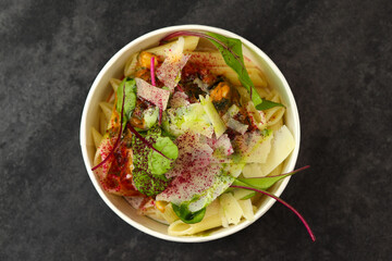 Pasta with mussels, cream sauce, parmesan and greens in a round paper takeaway food container on a dark background. Concept of take-away and healthy food delivery. Close-up, top view.
